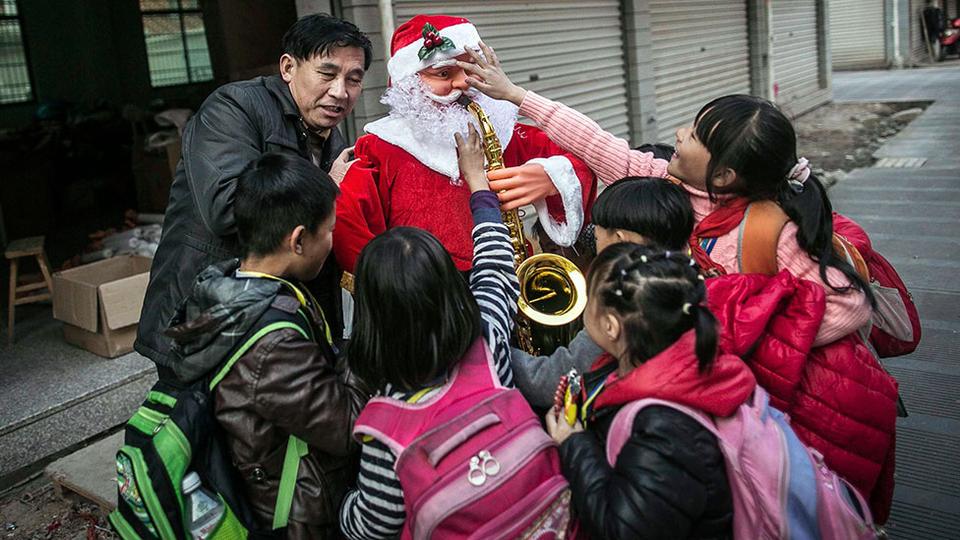 Worker holding a newly made Santa Claus model is surrounded by students in Yiwu