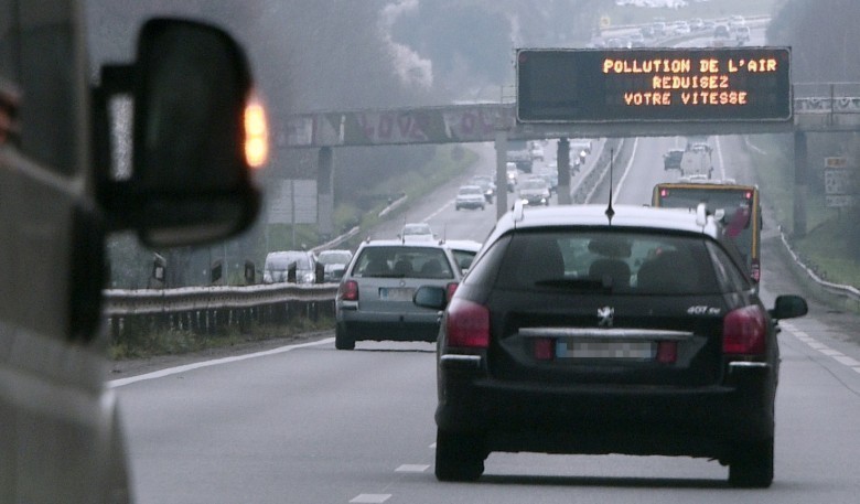 Motorists drive under a traffic board reading "Air pollution, slow down" near Rennes, western France, on March 21 , 2015.  Smog blowing in Europe, mixing with home-grown pollution, has been sending air pollution levels soaring, as French authorities will on March 23 put in place emergency traffic-limiting measures in Paris, as the City of Light and much of northern France suffers from a choking smog. AFP PHOTO / DAMIEN MEYER